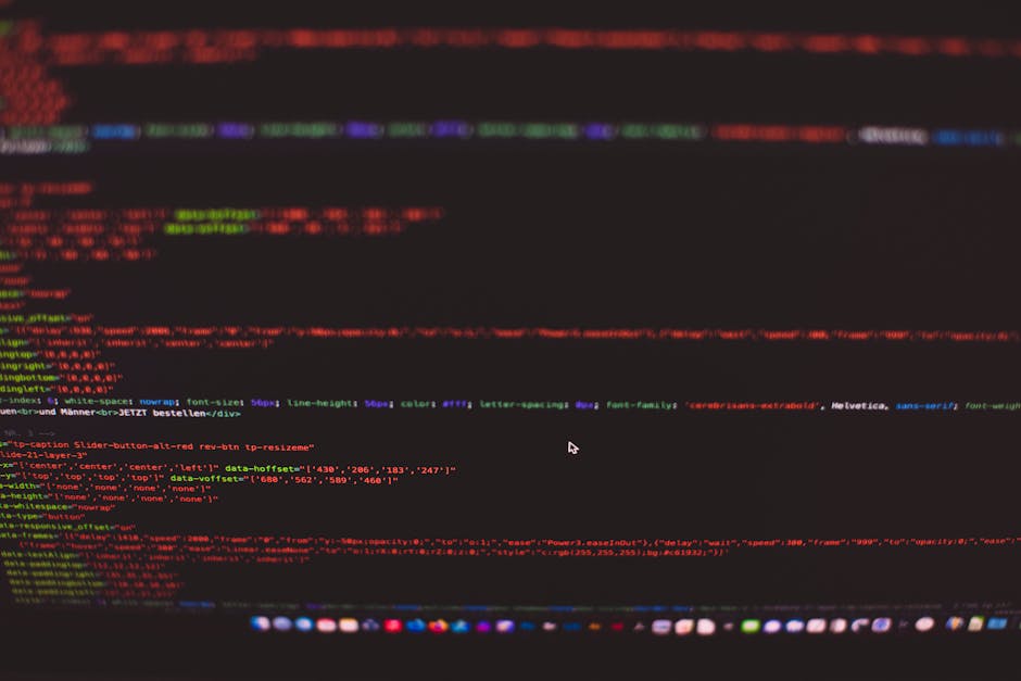 A close-up view of a computer screen displaying lines of colorful code on a black background, with red, green, blue, and purple syntax highlighting. The screen appears slightly blurred, emphasizing th